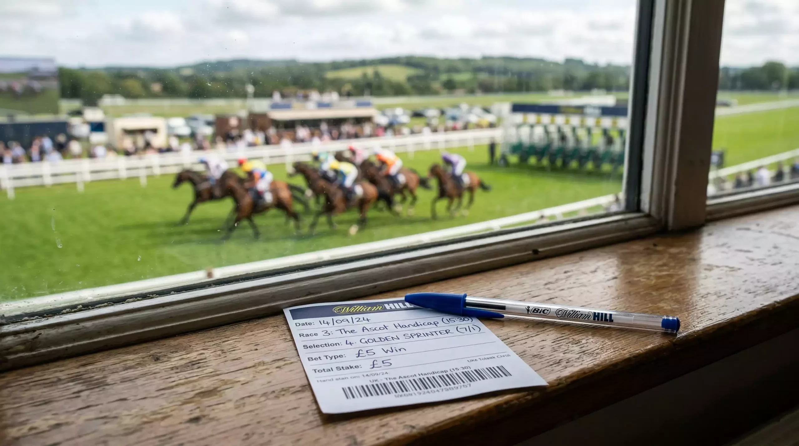Betting slip and pen on a racecourse table with horses visible in the distance