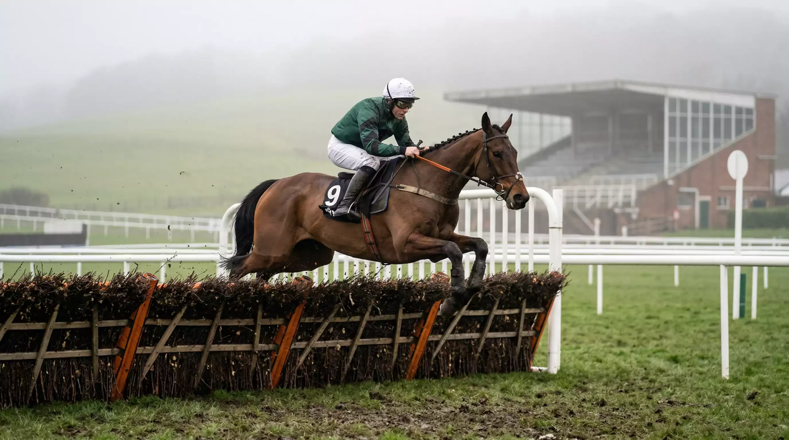 Horse and jockey clearing a hurdle on a misty National Hunt racecourse