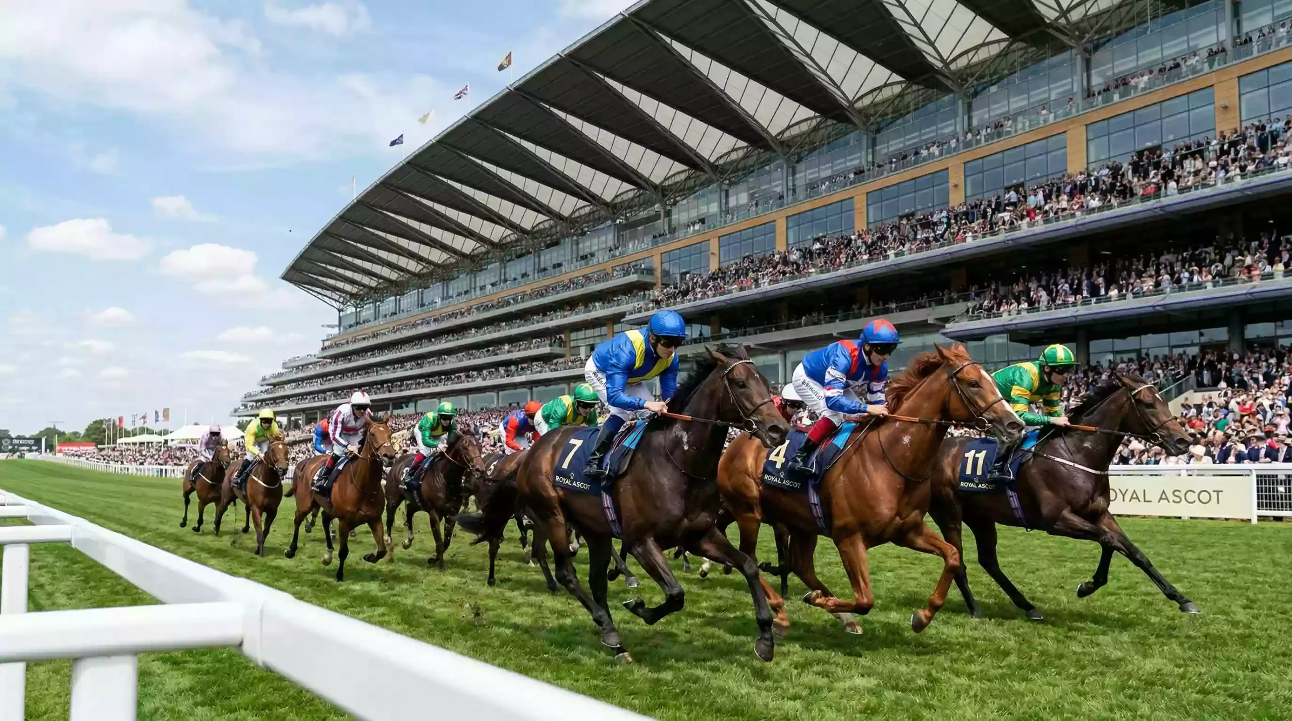 Flat racing action on the straight course at Royal Ascot with the grandstand behind